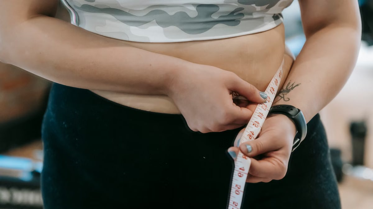 Crop anonymous plus size female with measuring tape measuring waist on blurred background